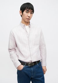 Lys rosa og hvit stripete skjorte med knapper og brystlomme, kombinert med blå jeans og svart belte. Glatt stoff, standard krage.