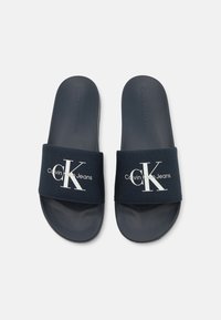 Marineblå sandaler med teksturert stoffrem som har en hvit logo. Flatsåle med jevn finish, designet for uformell bruk.