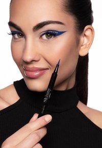 Penna per eyeliner nero tenuta da una persona, con punta sottile e linea decorativa blu sull'occhio. La persona ha pelle liscia e labbra lucide.