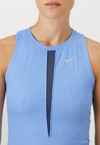 Canotta sportiva senza maniche di colore azzurro chiaro con texture a costine verticali, dotata di un pannello a forma di U di colore blu navy e un piccolo logo Nike argentato sul petto.