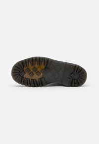 Sole in gomma nera con un profondo motivo di battistrada, caratterizzata da lugs di trazione esagonali e a forma di stella, e un'area della punta liscia con una leggera lucentezza.