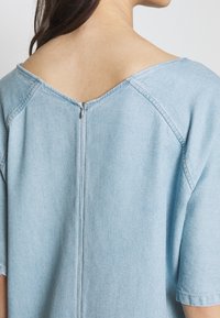 Jasnoniebieski denimowy top z szerokim dekoltem w serek i krótkimi rękawami. Posiada widoczny zamek błyskawiczny na plecach oraz miękkie, teksturowane wykończenie.