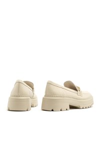 Beige leather loafers with a chunky beige platform sole, featuring a stitched detail and gold hardware accent on the side. Rounded toe design.