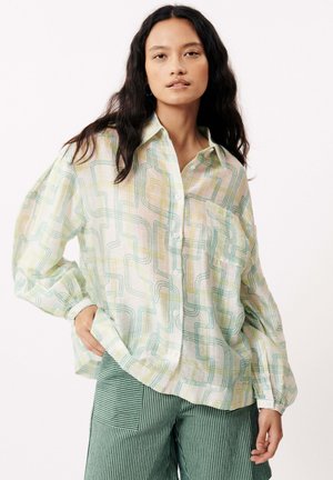 Chemise légère et transparente à boutons avec une coupe fluide. Présente un motif géométrique multicolore en vert, jaune et crème. Détail d'une poche.