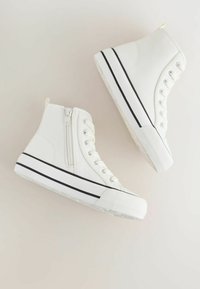 Baskets montantes blanches avec une tige en toile, des accents noirs, une fermeture éclair latérale et une semelle en caoutchouc contrastante. Design épuré et texture minimale.