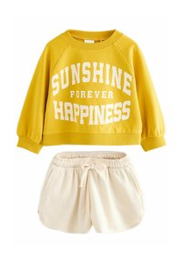 Gelbes Sweatshirt mit dem Text "SUNSHINE FOREVER HAPPINESS" in Weiß, kombiniert mit cremefarbenen Shorts mit elastischem Bund und Kordelzug.