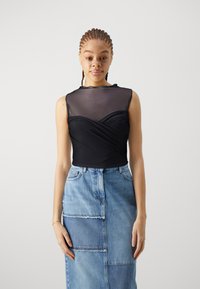 Sort med ermeløs topp med teksturert mesh overlag og design med omslag foran, sammen med en lyseblå jeansskjørt med lappverk.
