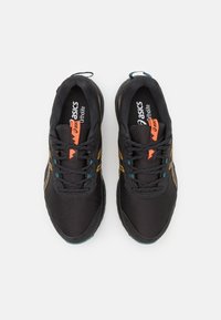 Baskets de sport noires avec tissu en maille, accents orange et turquoise, bout arrondi et lacets ajustables. Logo affiché sur la semelle intérieure.