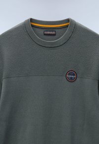 Maglione grigio con texture, dotato di scollatura rotonda, caratterizzato da una parte inferiore liscia, colletto a coste e una toppa circolare con logo in blu navy e arancione.