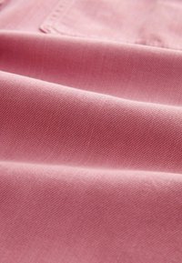 Tejido de mezclilla rosa con un fino tejido de sarga, con una textura suave y costuras visibles, que muestra pliegues suaves y caída.