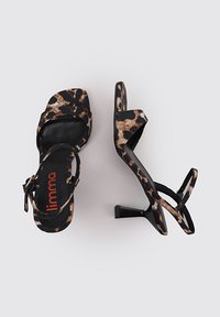 Sandalias de tacón alto con estampado de leopardo en negro y beige, con punta abierta, una delgada correa en el tobillo y un tacón cuadrado texturizado. Logo de la marca visible.