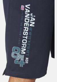 Marineblaue Baumwollshorts mit besticktem Text, darunter "JAN VANDERSTORM" und Koordinaten, sowie seitlichen Schlitzen für Bewegungsfreiheit.