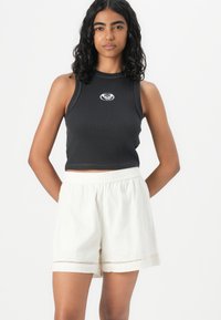 Black ribbed crop top with a white embroidered logo, paired with light-colored shorts featuring a lace trim at the hem.