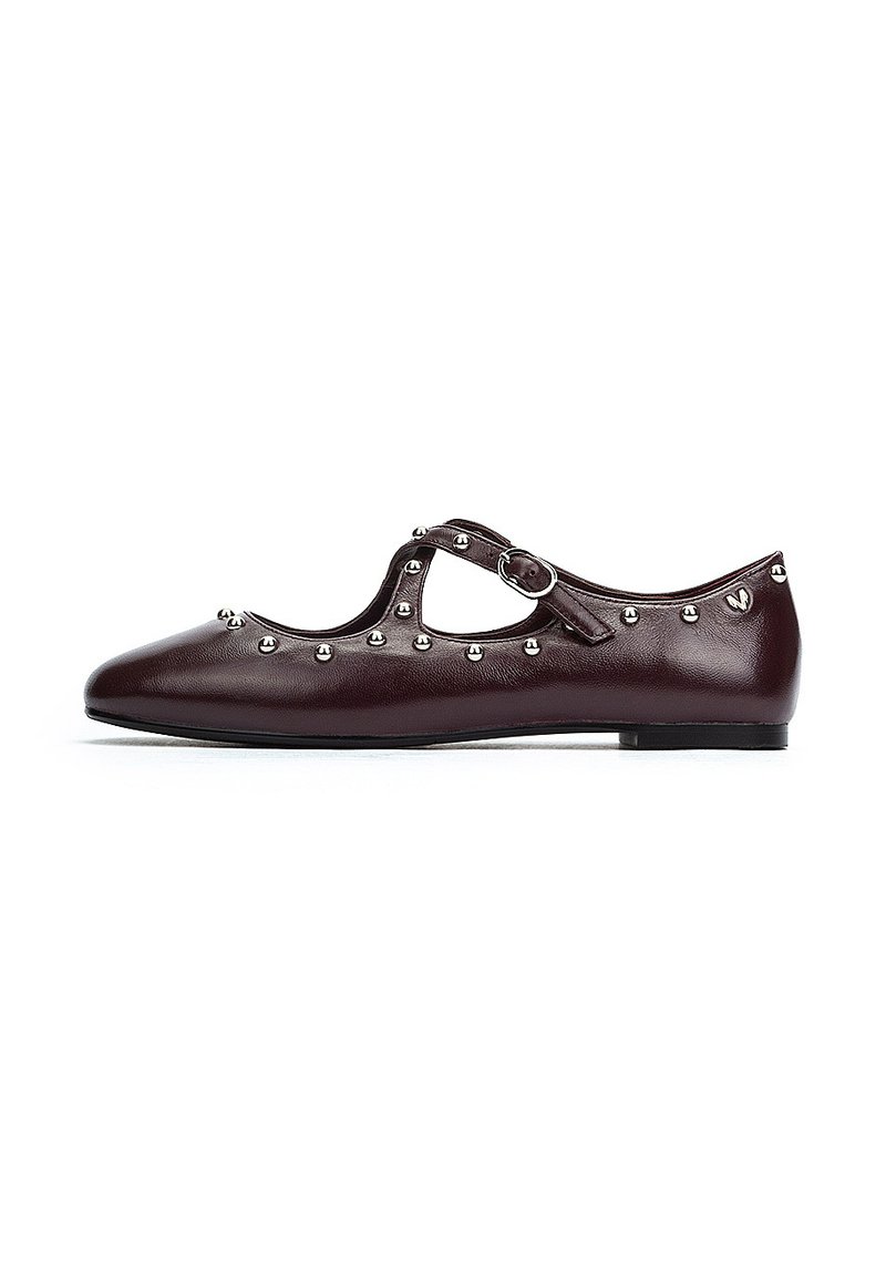 Zapato plano de cuero burdeos con punta redonda, tira de tobillo, tachuelas plateadas en el borde y una textura suave.