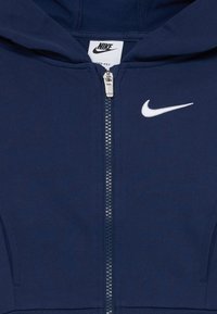 Sweat à zip navy en tissu doux, doté d'un logo Nike blanc sur la poitrine gauche, d'une capuche ajustable et de poignets côtelés.