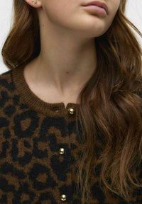 Kardigan i ullblandning med brun och svart leopardskrivning, rund hals och knappar i guldton. Mjuk textur med ribbat krage.