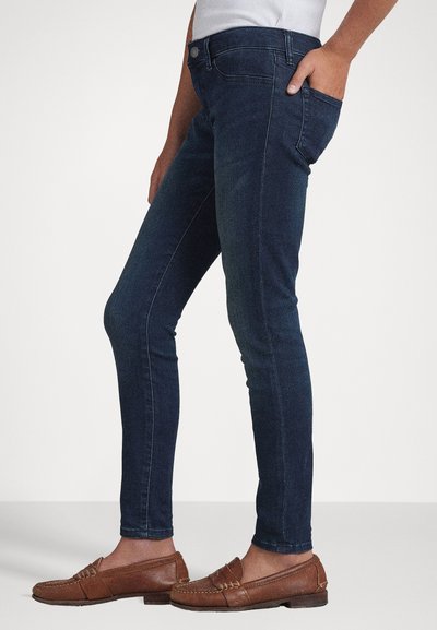 Jeans ajustados de algodón denim de color azul oscuro, con una cintura de altura media, bolsillos laterales y una textura suave. Combinados con mocasines marrones.
