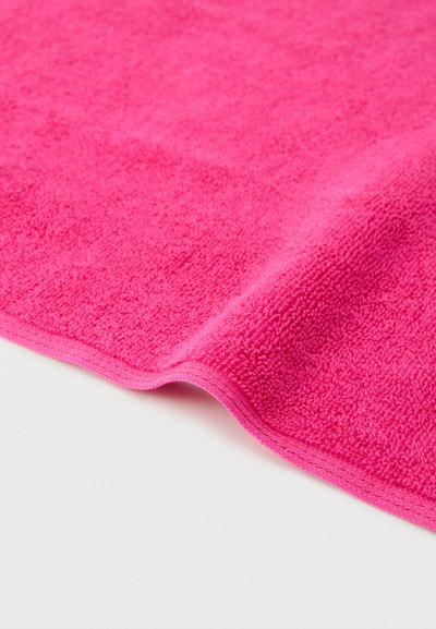 Φωτεινή ροζ πετσέτα από περκάλι υφασμένη σε λευκή επιφάνεια, δείχνοντας την υφή και τους μαλακούς θύσαυρους υφάσματος.