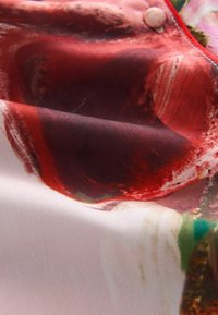 Zijde stof met een kleurrijk abstract patroon van rode, roze en groene wervelingen. De textuur is glad met een lichte glans.