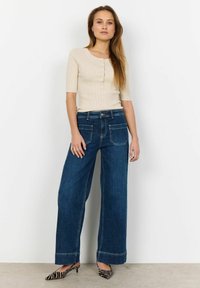 Beige ribbat kortärmad topp med knäppning, i kombination med vida mörkblå denimjeans med dubbel sömnad. Svart- och vitrandiga klackar.