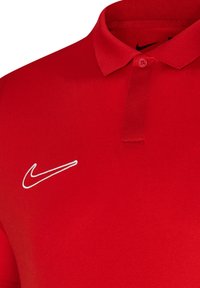 Polo rouge uni ; il présente un col classique, une fermeture à boutons et un logo Nike blanc brodé sur le côté gauche.