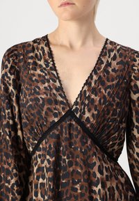 Vestido de padrão de leopardo em tons de castanho e preto. Apresenta um decote em V profundo, tecido plissado e uma delicada renda preta ao longo da gola.
