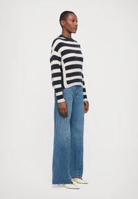 Un pull en tricot rayé bleu marine et crème, associé à un jean bleu à taille haute et jambes larges. Les fibres semblent douces avec une coupe décontractée.
