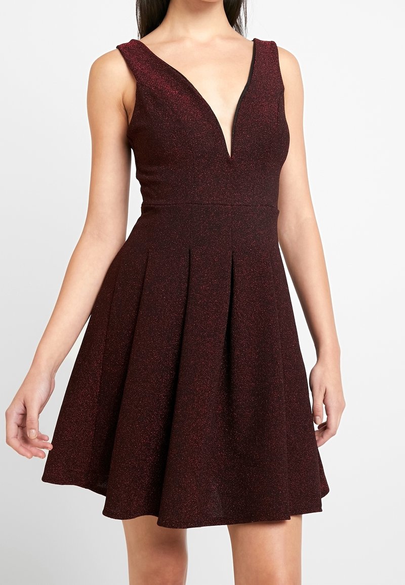 Robe bordeaux évasée avec un décolleté en V profond, sans manches, et une texture subtilement scintillante. Jupe plissée pour plus de volume.