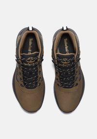 Zapatos de senderismo marrones con acentos de malla negra, cuero texturizado y cordones reflectantes, que cuentan con una suela robusta y la marca Timberland.