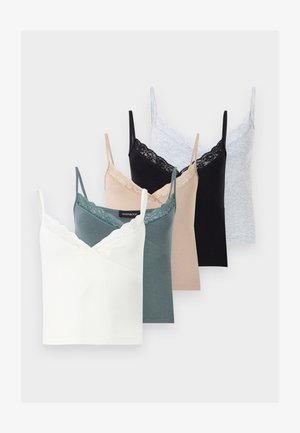 Jeune femme portant un caraco noir bordé de dentelle, un pantalon cargo gris, des talons noirs pointus, tenant un sac à épaule noir sur fond blanc.