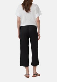 Witte linnen crop top met korte mouwen, gecombineerd met zwarte wijde broek en bruine platte sandalen. Eenvoudig ontwerp en neutrale kleuren.