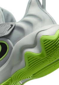 Zapatilla gris claro con parte superior de tela texturizada, logotipo negro y suela verde brillante con diseño ondulado y patrones de tracción distintivos.