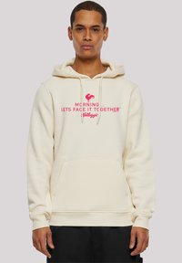 Beige Kapuzenpullover mit einer Fronttasche, der ein pinkes Grafiktextdesign mit der Aufschrift "MORNING ... LET'S FACE IT TOGETHER™ KELLOGG'S" zeigt.