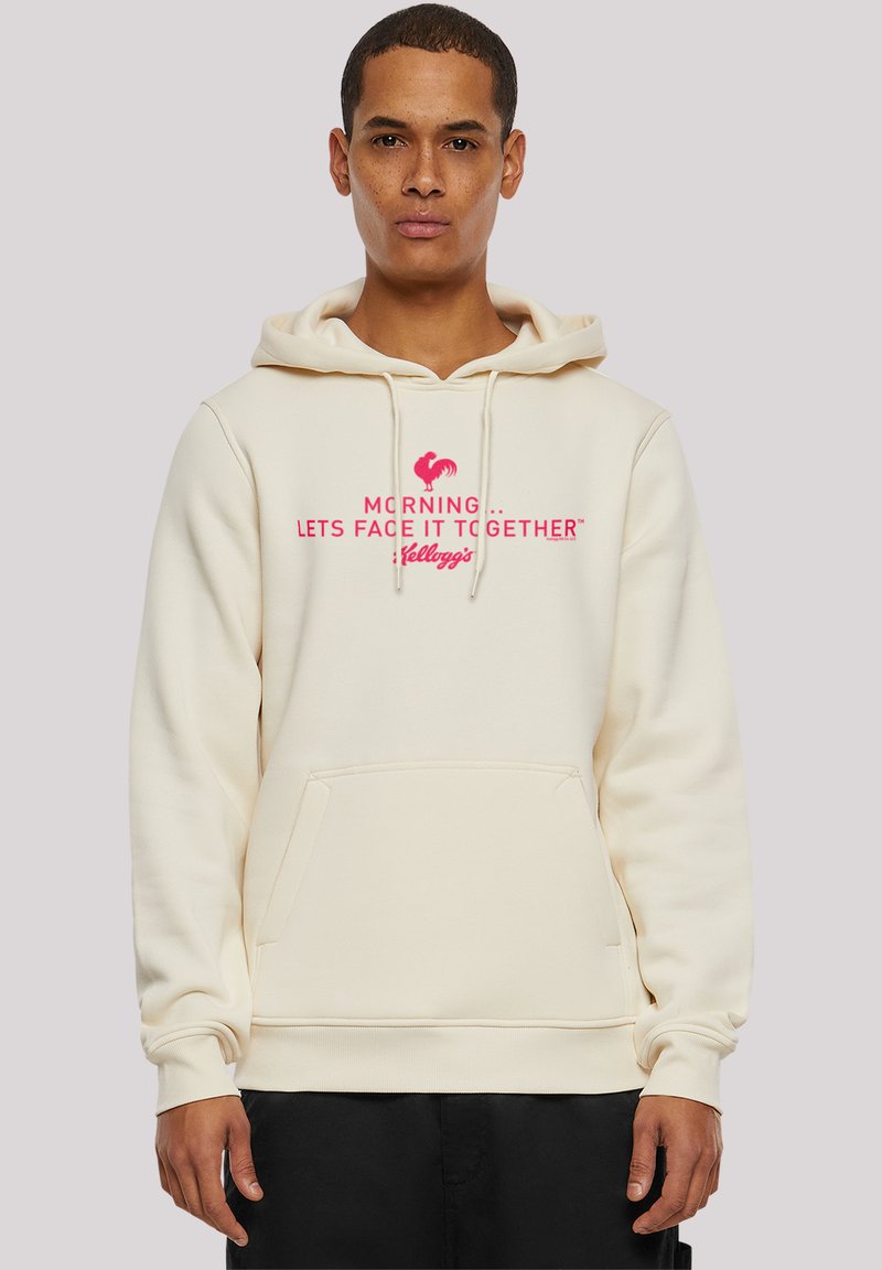 Beige Kapuzenpullover mit einer Fronttasche, der ein pinkes Grafiktextdesign mit der Aufschrift "MORNING ... LET'S FACE IT TOGETHER™ KELLOGG'S" zeigt.