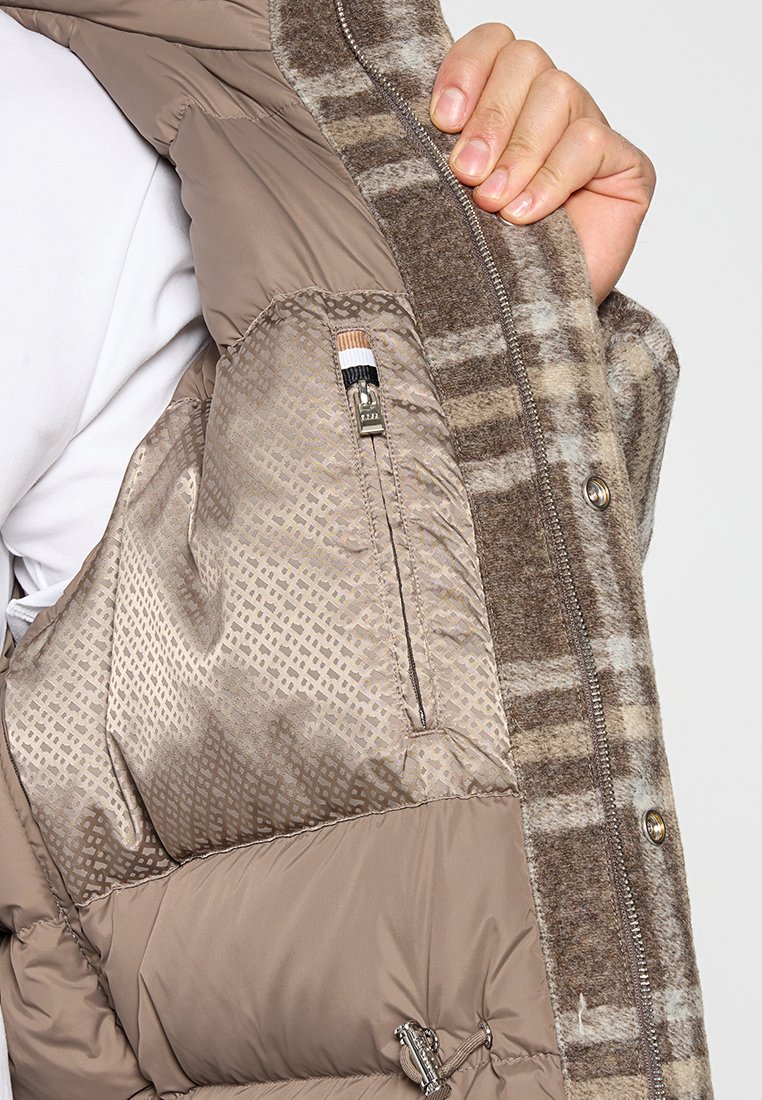 Veste brune rembourrée avec un intérieur à motifs et une poche zippée. Le tissu extérieur présente un motif à carreaux brun et beige.