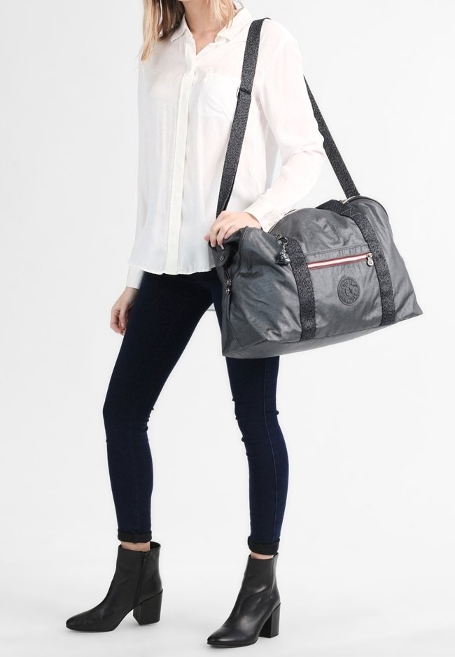 Šedá duffel taška s černými vzorovanými popruhy, zipovým uzávěrem a detailem loga. Měkký, lehký materiál s prostorným designem.