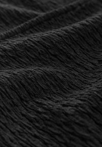 Mustast kangast, millel on kortsus muster, mis näitab kootud disaini ja erinevaid pinna sügavusi. Pehme, kerge ja painduv materjal.