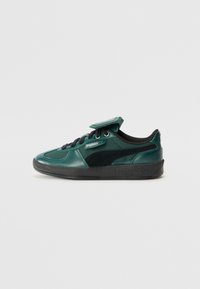 Zapatilla deportiva verde de ante y sintética con detalles en negro, punta redonda, diseño con cordones y lengüeta acolchada con parche de logo. Suela de goma.