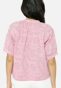 Rozā kokvilnas blūze ar īsām pūkām, ar ziedu izšuvumu un savilkta apkakle. Gluda tekstūra, brīva piegriezuma un vienkārša muguras dizains.