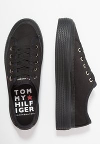 Schwarze Tommy Hilfiger Low-Top Sneaker mit dicken Gummisohlen und schwarzen Schnürsenkeln, aus der Draufsicht und der Seitenansicht auf einem weißen Hintergrund.