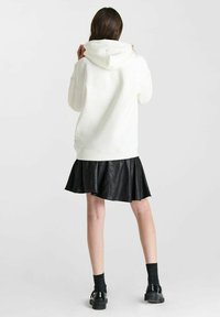 Witte hoodie met een ontspannen pasvorm, voorzien van een grote capuchon en geribbelde manchetten, gecombineerd met een zwarte nep leren rok en chunky zwarte schoenen.