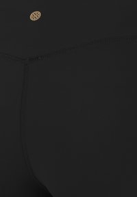 Shorts noirs en tissu lisse et extensible, avec des coutures plates. Un petit logo doré est placé sur la taille.