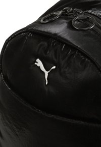 Zwarte leren rugzak met glanzende textuur, voorzien van dubbele ritsen en een wit Puma-logo. Gebogen vorm met een gladde oppervlakte.