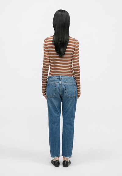 Pruunikirju pikkade varrukatega top, sinised sirge lõikega teksapüksid ja mustad kingad. Komplekt on vabaaja stiilis ning sellel on nähtavad õmblustead.