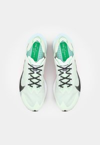 Des chaussures de course vert clair présentent une tige en maille respirante avec un motif en zigzag, des lacets noirs et un design de semelle courbée distinctif.