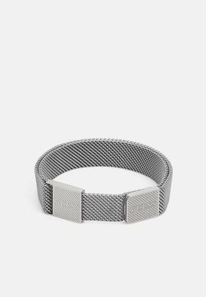 Silbernes Mesh-Armband mit zwei quadratischen Verschlüssen, graviert mit dem Markennamen Guess, auf einem einfarbigen weißen Hintergrund.