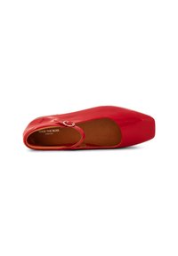 Zapato plano de charol rojo con punta cuadrada, que cuenta con una correa asegurada por un anillo metálico, textura suave y un forro interior color beige.