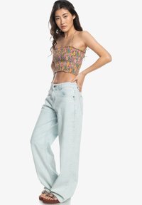 Bloemmotief cropped tanktop gecombineerd met lichtblauwe wijde jeans, voorzien van voortassen en een gladde textuur.