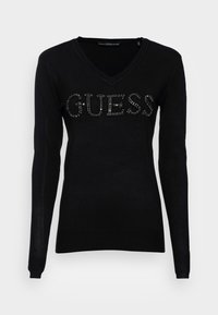 Mustat V-kaula-aukkoinen neulepaita pitkillä hihoilla ja etuosassa "GUESS" -logo strasseilla. Valmistettu pehmeästä, kevyestä kankaasta, jossa on ribbireunat.