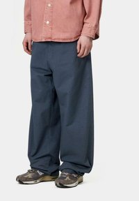 Pantalones de algodón azules anchos combinados con una camisa de botones rosa, que presenta un corte relajado y una textura sutil. El calzado son zapatillas con un diseño estampado.
